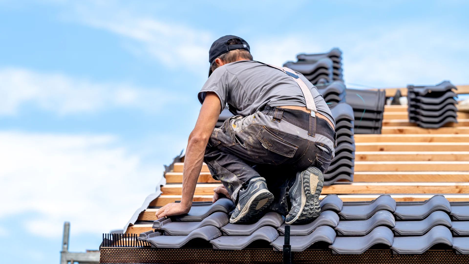 Dachdecker kniet auf der Dachlattung und verlegt Dachziegel bei einem Neubau