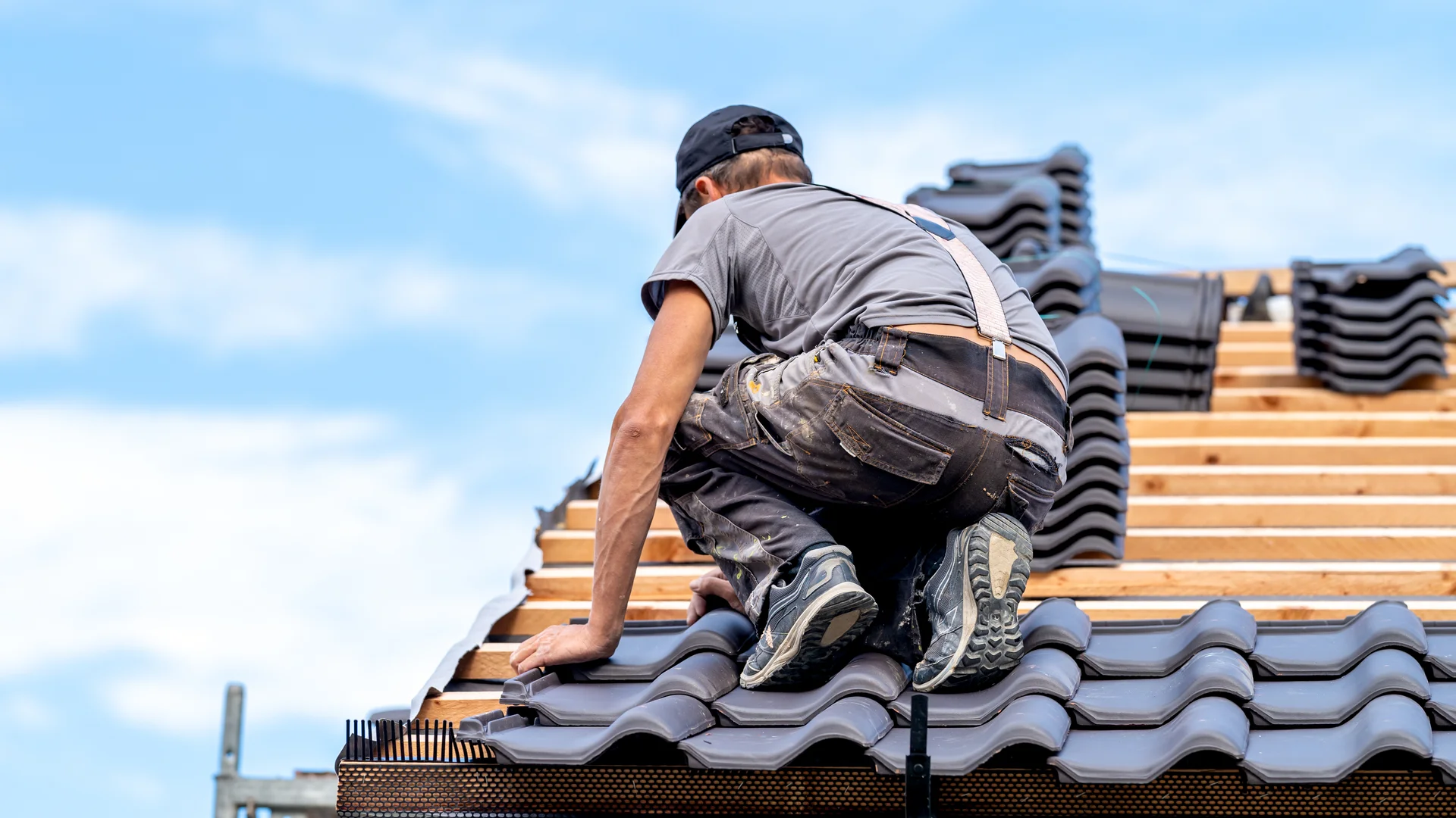 Dachdecker kniet auf der Dachlattung und verlegt Dachziegel bei einem Neubau