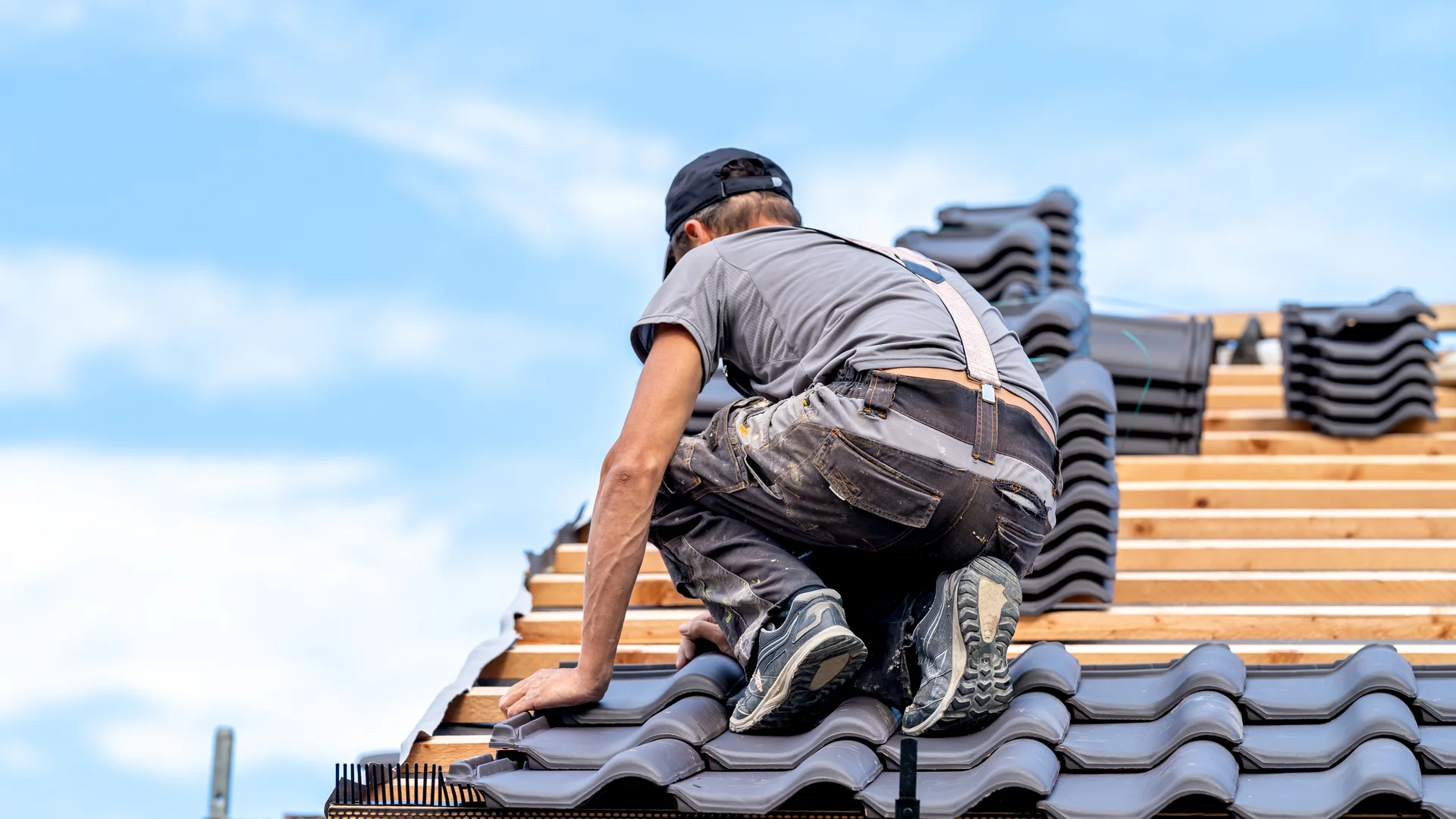 Dachdecker kniet auf der Dachlattung und verlegt Dachziegel bei einem Neubau